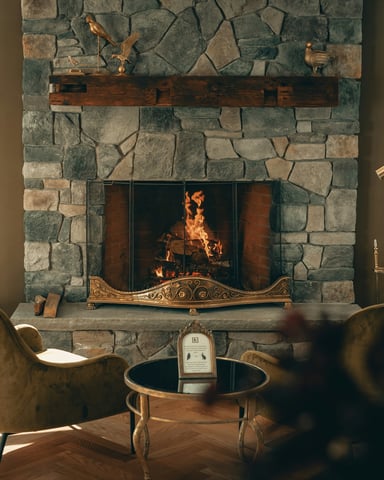 Stone fireplace with roaring fire and velvet armchairs in a warm lodge sitting room