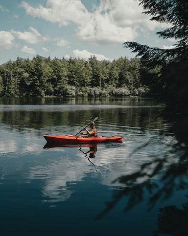 Solo kayaker on a still forest lake under a cloudy summer sky
