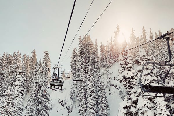 Chairlift rising through snow-covered pine trees with warm winter backlight