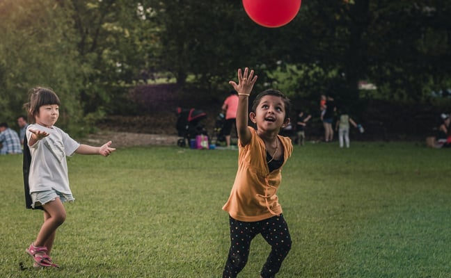 Two kids playing with a ball on a sunny green lawn