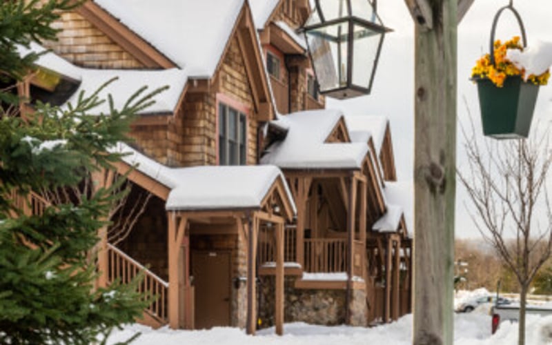 Wooden cottage with snow-covered peaked roofs and hanging flower basket on lamp post