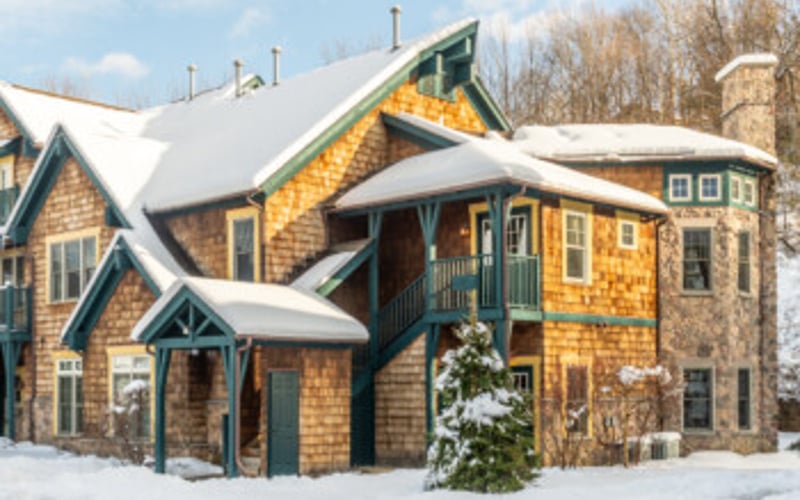 Stone and wood cottage with snow-covered roof and chimney in winter landscape