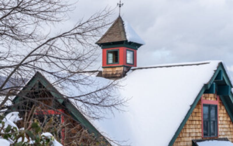 Red and gold church steeple with cross rising above snow-covered roofs and bare branches