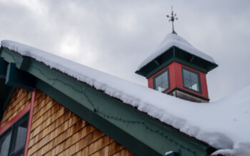 Red and green cupola with cross on snowy roof of wooden building