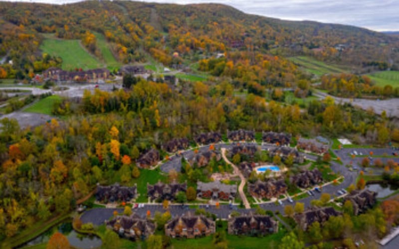 Aerial view of suburban neighborhood nestled in forested valley with autumn foliage and winding roads