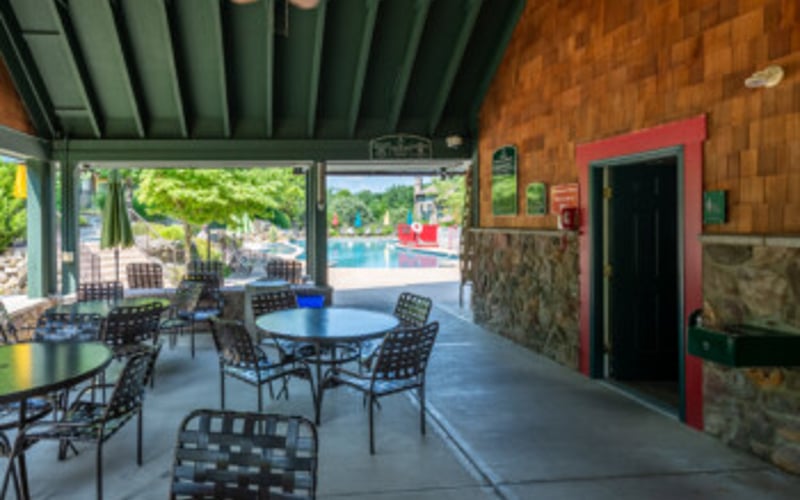 Covered patio with blue round table, black chairs, and view of garden and pool area