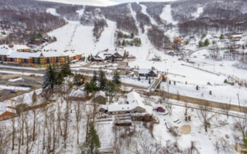 Aerial view of ski resort with snowy slopes, lodge buildings, and forested terrain in winter