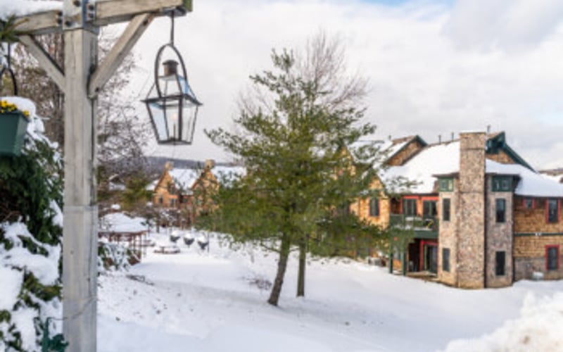 Snow-covered courtyard with lantern hanging from wooden beam and brick buildings in background