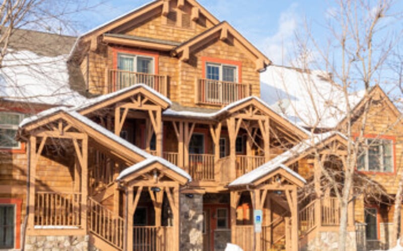 Large wooden house with multiple peaked roofs and wraparound porches in winter setting