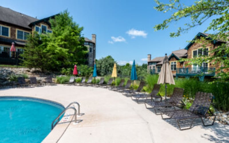 Resort pool with lounge chairs and umbrellas, residential buildings and landscaping in background
