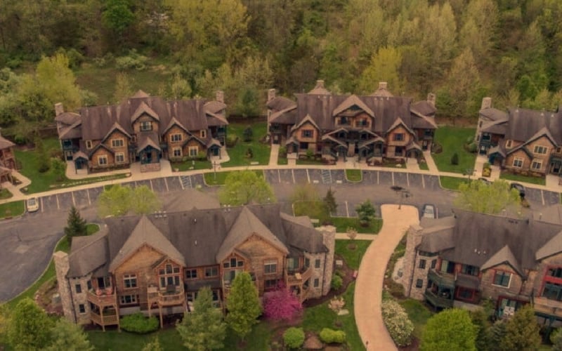 Aerial view of residential community with large brick homes, curved streets, and forested surroundings