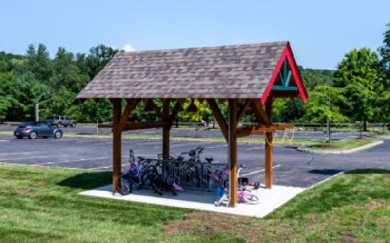 Red-roofed wooden pavilion with motorcycle parking in grassy park area