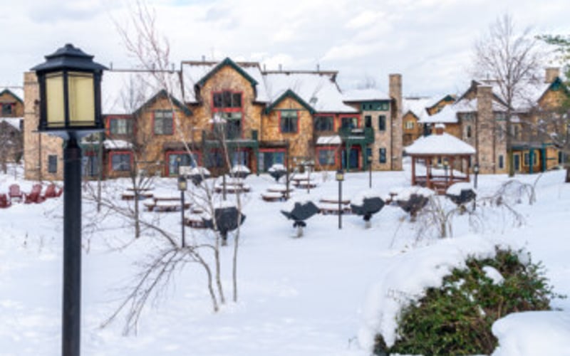 Stone and brick buildings in snowy village square with bare trees and street lamp