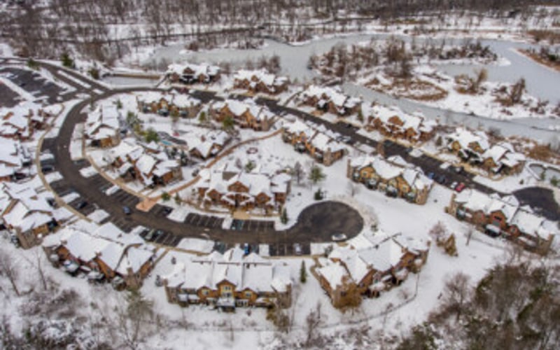 Aerial view of suburban neighborhood with curved streets and houses surrounded by snow-covered forest