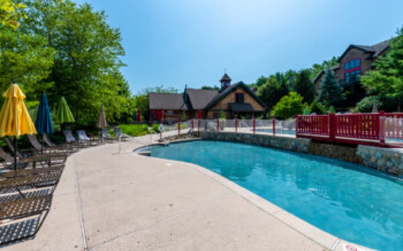 Resort swimming pool with concrete deck, lounge chairs, and red fence bordering residential buildings