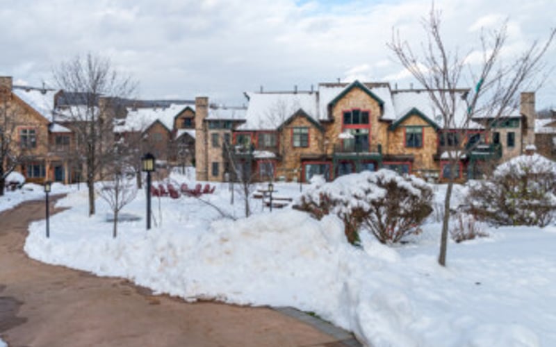 Snow-covered town square with yellow stone buildings and bare trees in winter
