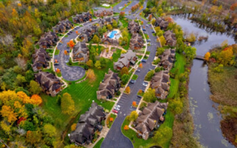 Aerial view of suburban neighborhood with curved streets, houses, and surrounding wetlands and autumn trees
