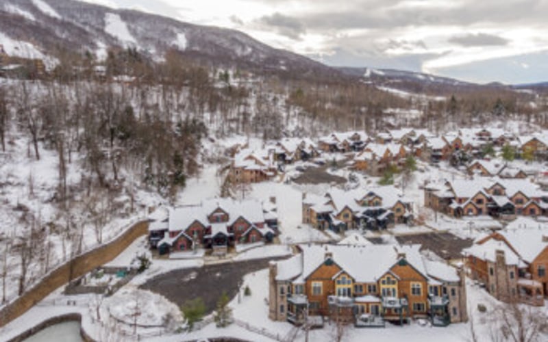Snowy mountain village with winding road, residential buildings, and forested hillside in winter