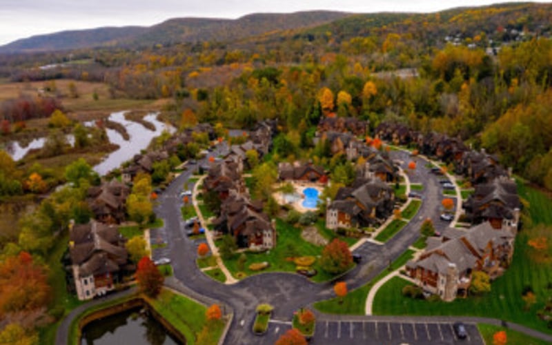 Aerial view of residential neighborhood with curved streets, houses, and central pool surrounded by autumn trees and winding river