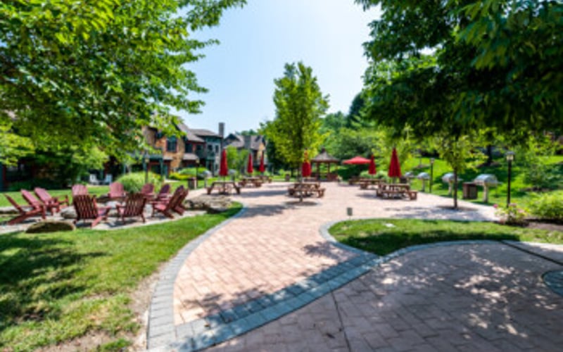 Brick patio with seating areas surrounded by mature trees and green lawn in residential garden