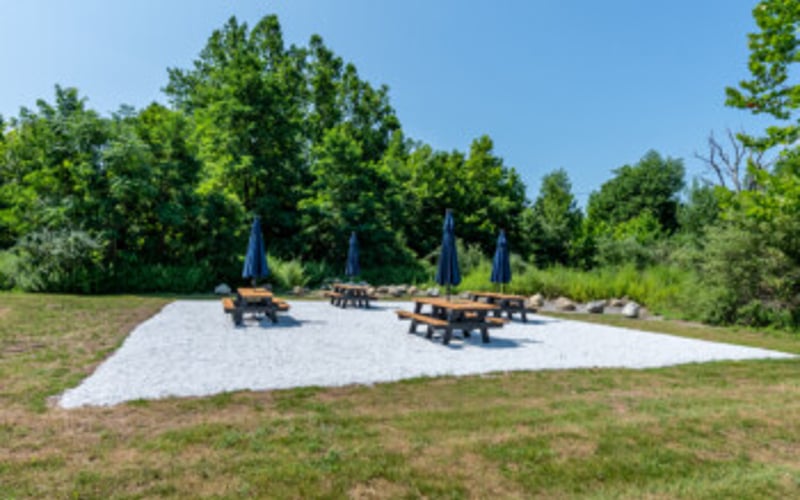 Outdoor playground with blue umbrellas and equipment on white surface surrounded by green trees